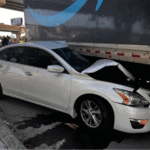 Passenger car with severe front-end damage after sliding under the side of a commercial truck trailer in an underride crash
