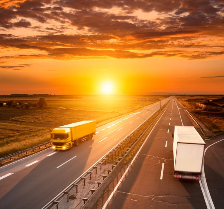Two commercial semi-trucks traveling in opposite directions on a divided highway at sunset with a dramatic orange sky, representing the heavy truck traffic on texas roads handled by a truck accident law firm.