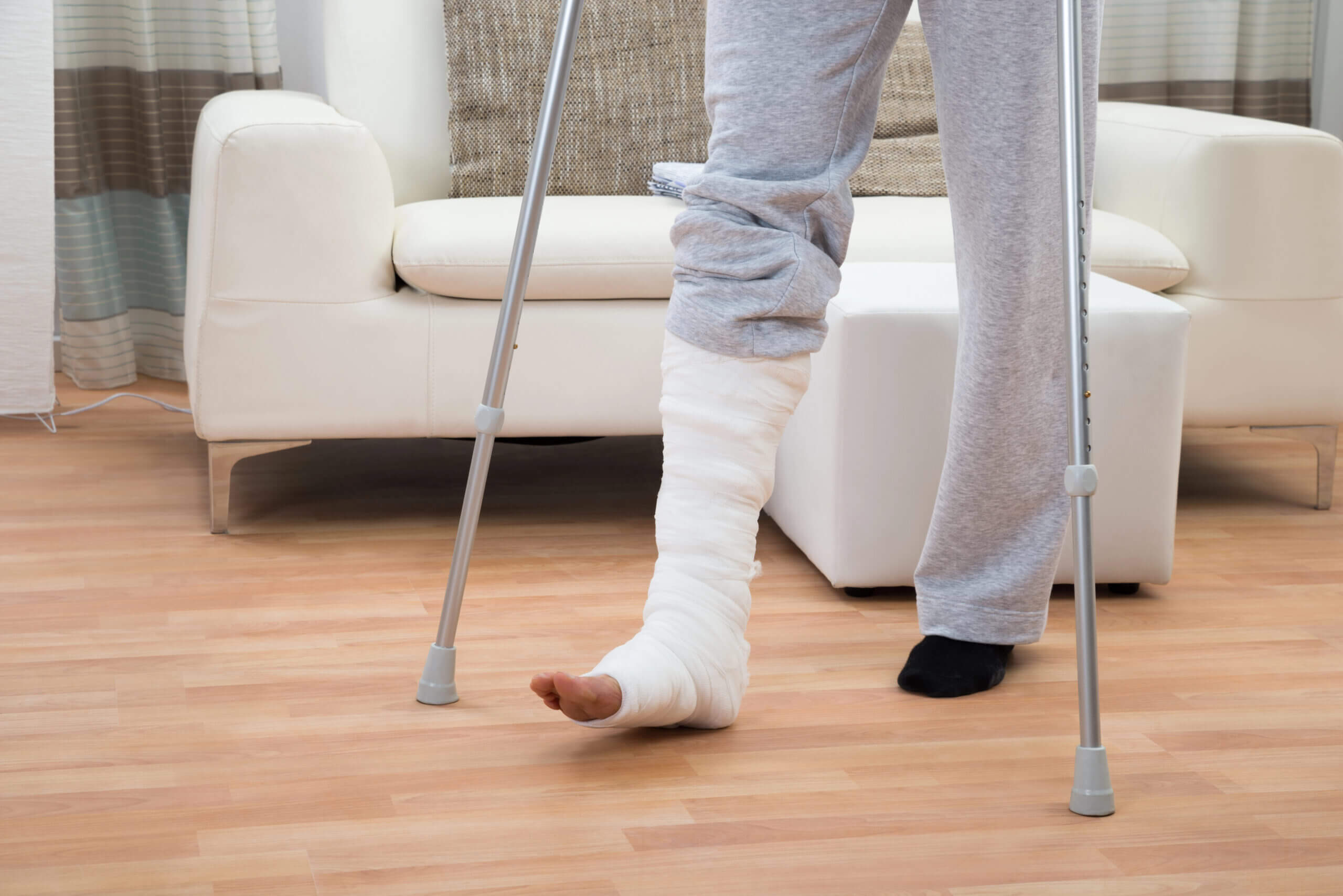 A truck accident injury victim walking on crutches at home with a full leg cast, representing the broken bones and long recovery period caused by serious commercial truck crashes.